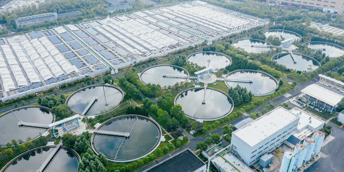 Aerial view of an ecological transformation facility with water treatment basins and solar-roofed complex